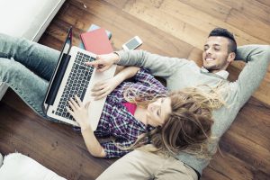Couple shopping online at laptop computer - Two young friends watching a video on a notebook in the living room, view from above